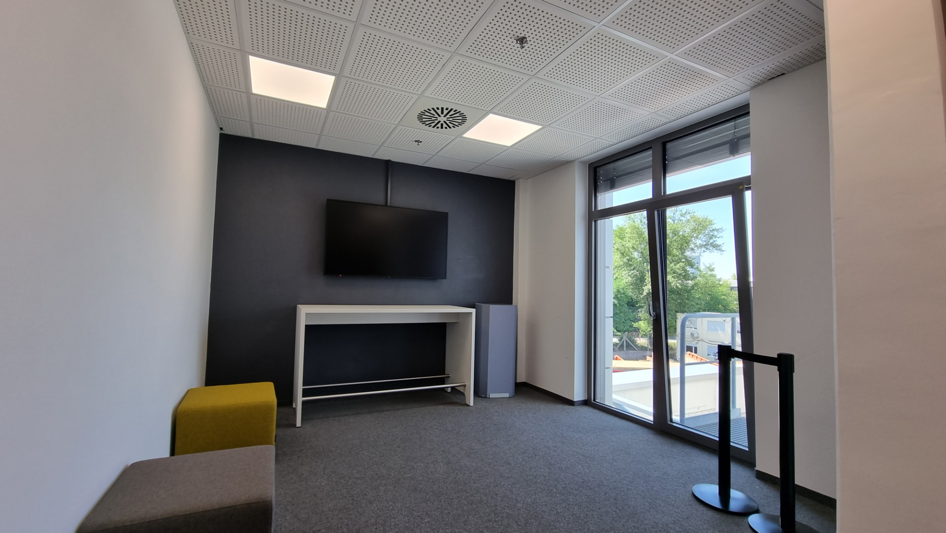 Modernes Büro mit dunkler TV-Wand und gelber Hocker-Sitzbank