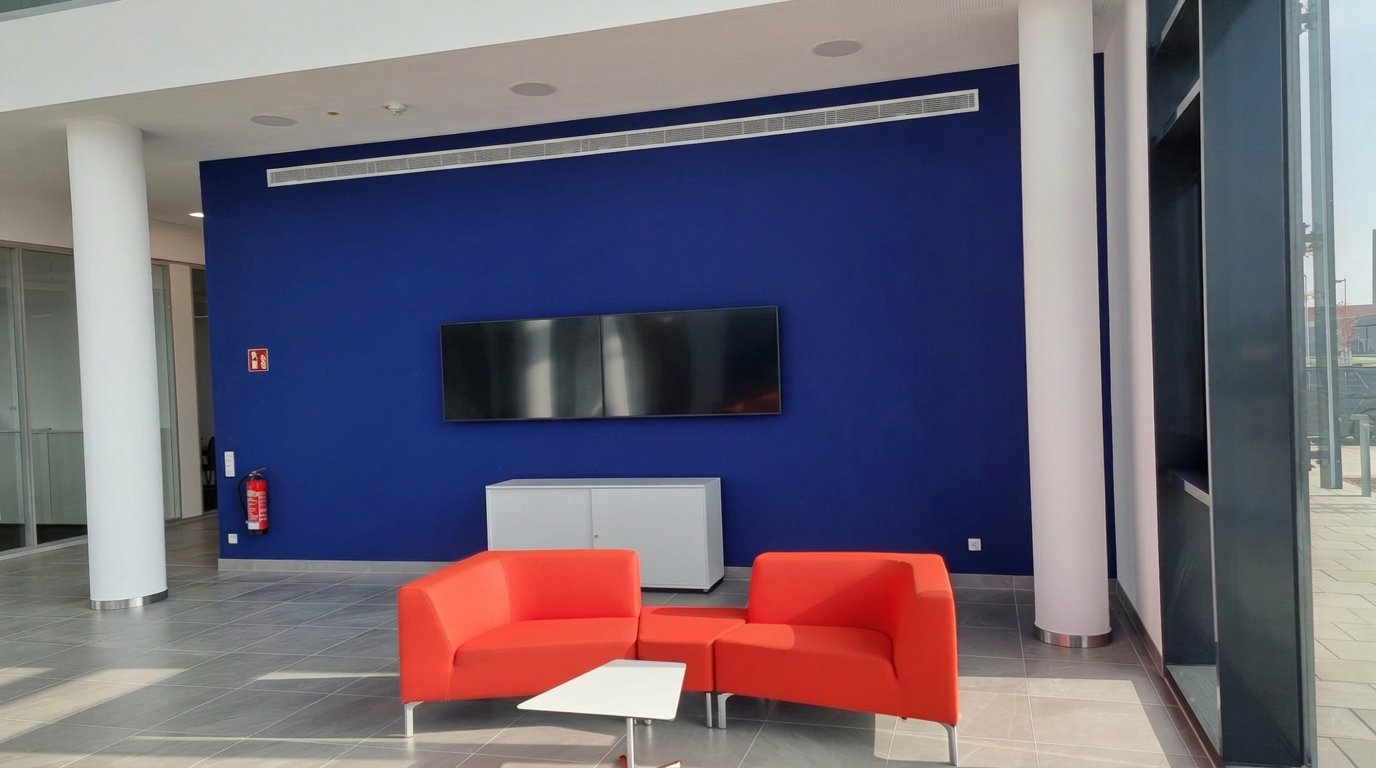 Empfangsbereich mit blauer Akzentwand, Wandmonitoren und roten Sitzinseln
